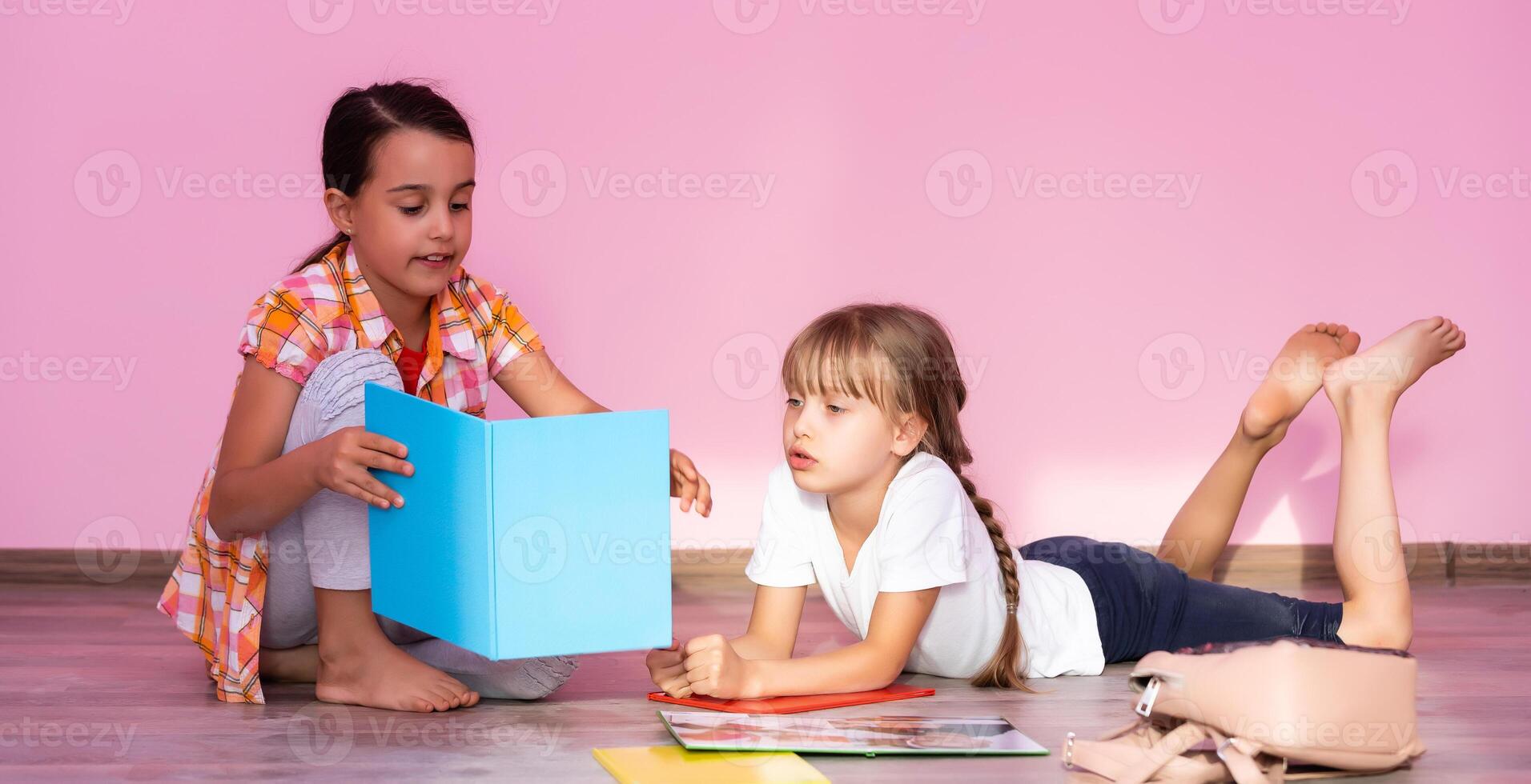 weinig meisjes lezing een boek in leven kamer. slim schoolmeisjes aan het doen hun huiswerk na school. onderwijs en afstand aan het leren voor kinderen. thuisonderwijs gedurende quarantaine. blijven Bij huis amusement. foto