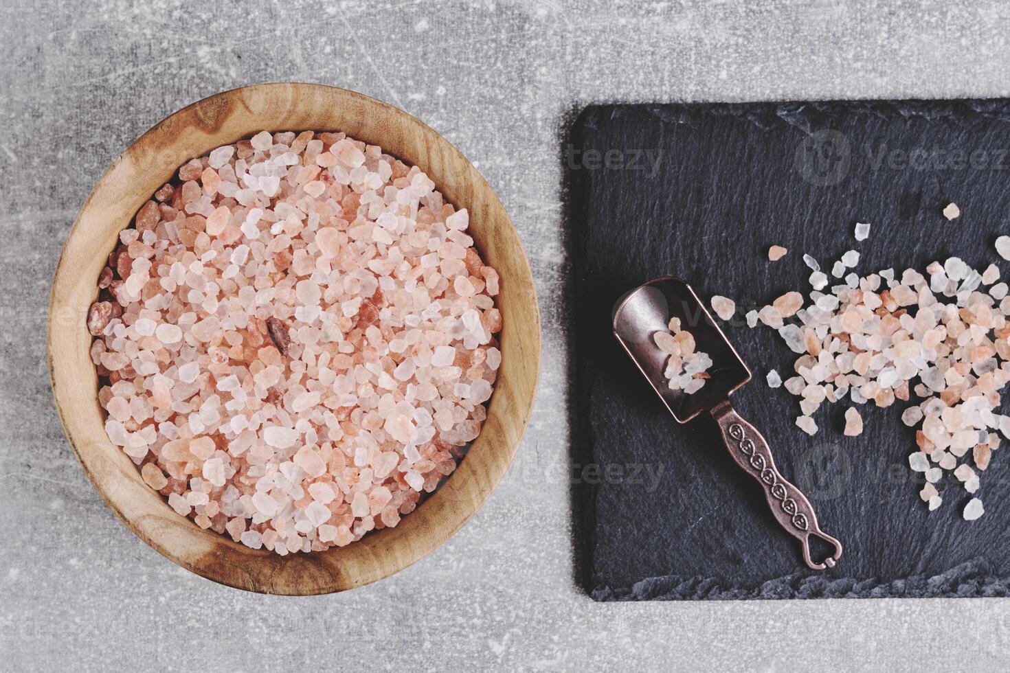 roze himalayan zout in houten kop en een kruid lepel Aan een leisteen steen achtergrond. foto