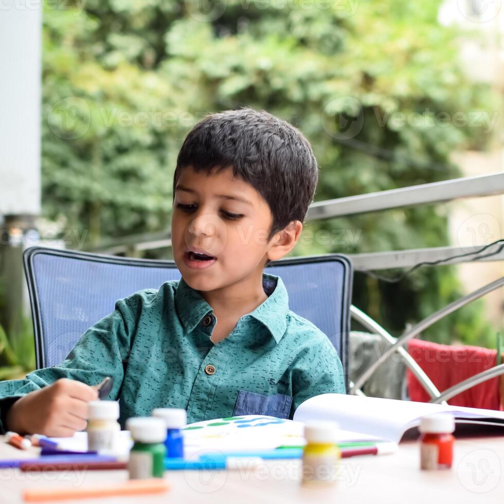 slim Indisch weinig jongen uitvoeren duim schilderij met verschillend kleurrijk water kleur uitrusting gedurende de zomer vakanties, schattig Indisch kind aan het doen kleurrijk duim schilderij tekening Aan houten tafel foto