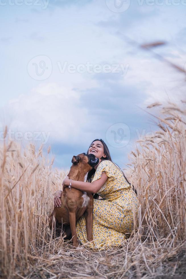 gelukkige jonge man die zijn hond knuffelt terwijl hij samen geniet van de dag buiten in een tarweveld. foto