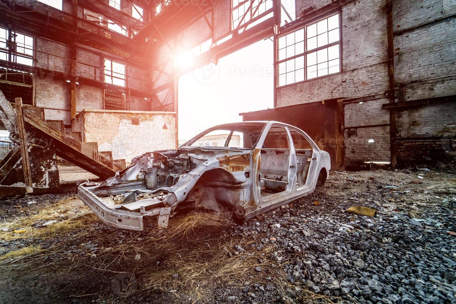 metaal kader van een roestig auto in een groot oud verlaten gebouw binnen met licht lekt. gebroken en vergeten verroest auto kader Aan de achtergrond van geruïneerd fabriek foto