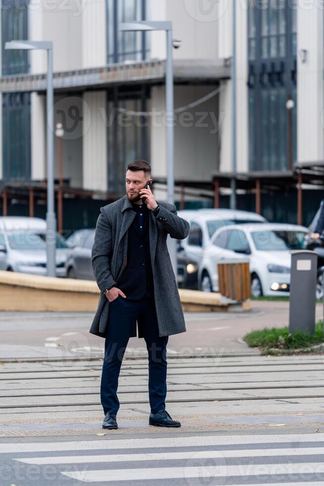 jong aantrekkelijk zakenman hebben een telefoon telefoontje Aan een modern straat. modieus Mens in gewoontjes kleding wandelen naar beneden de straat. foto