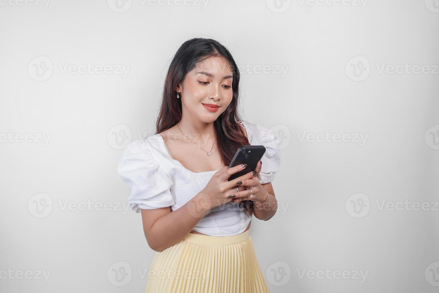 een vrolijk Aziatisch vrouw is glimlachen en Holding haar smartphone, geïsoleerd door wit achtergrond. foto