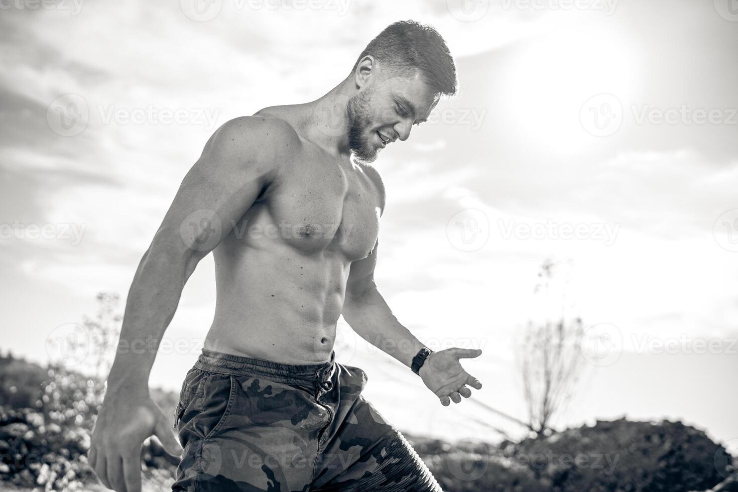 jong atletisch Mens staand Aan de steen. bodybuilder met naakt torso en vervelend camouflage broek. gezond en mooi lichaam in zwart en wit kleuren. foto