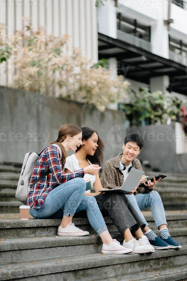 studenten zijn aan het studeren de campus park. jong mensen zijn uitgeven tijd samen. lezing boek, werken met laptop, tablet en communiceren terwijl foto