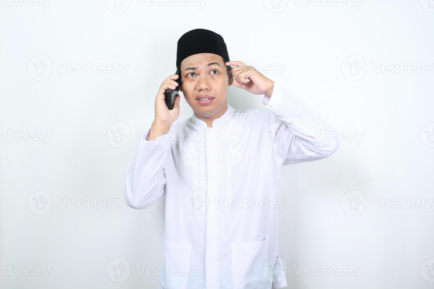 Aziatisch moslim Mens aanraken zijn hoofd tonen verward uitdrukking terwijl pratend Aan de telefoon geïsoleerd Aan wit achtergrond foto