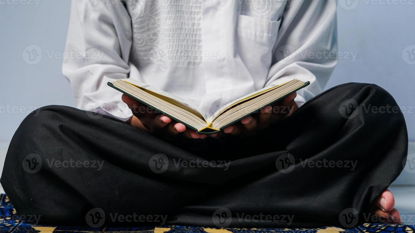 dichtbij omhoog van een moslim Mens zittend bidden en lezing de koran Aan een gebed mat. foto