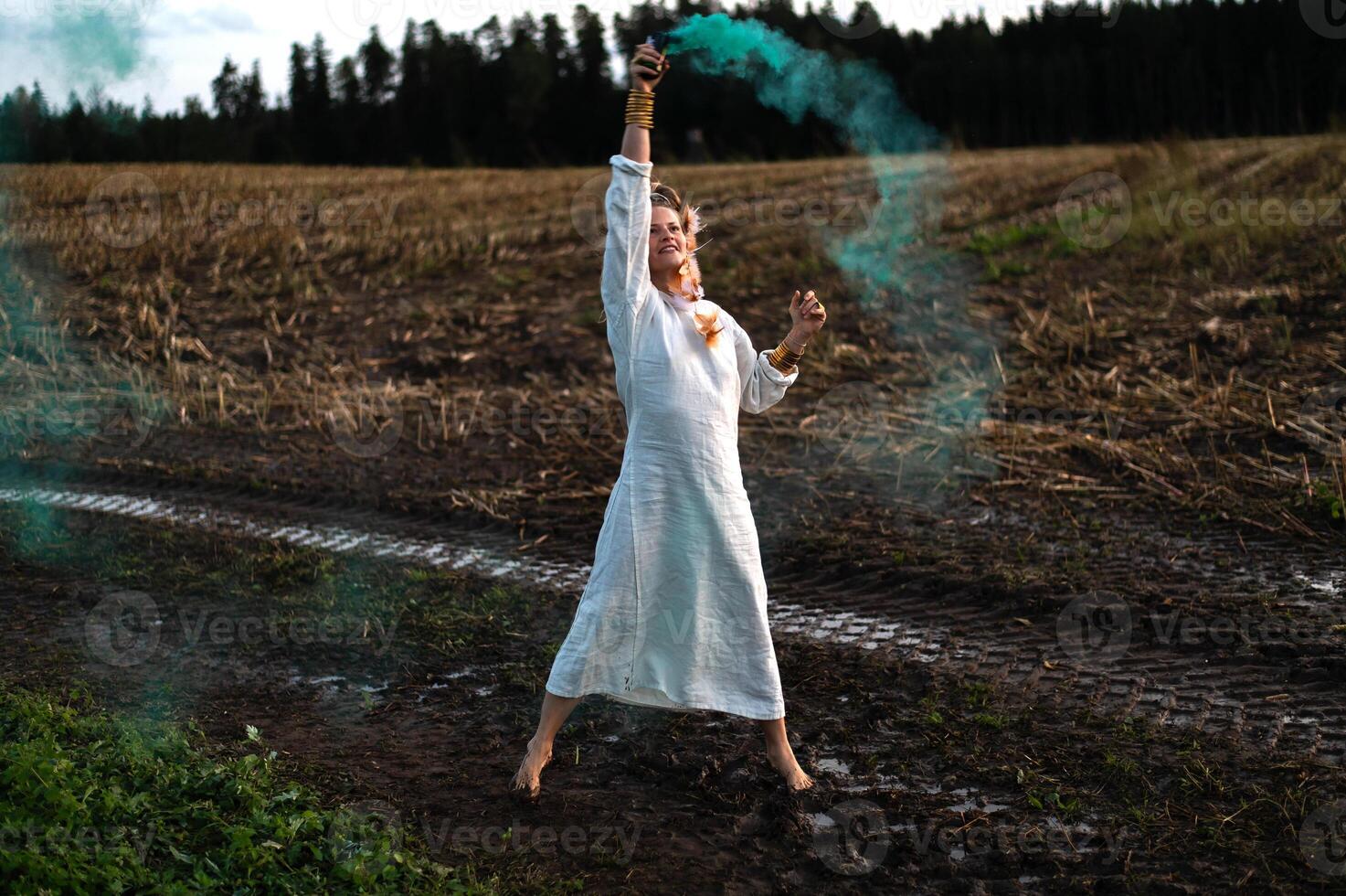 vrolijk jong vrouw met riet dansen in gekleurde rook in een veld- foto