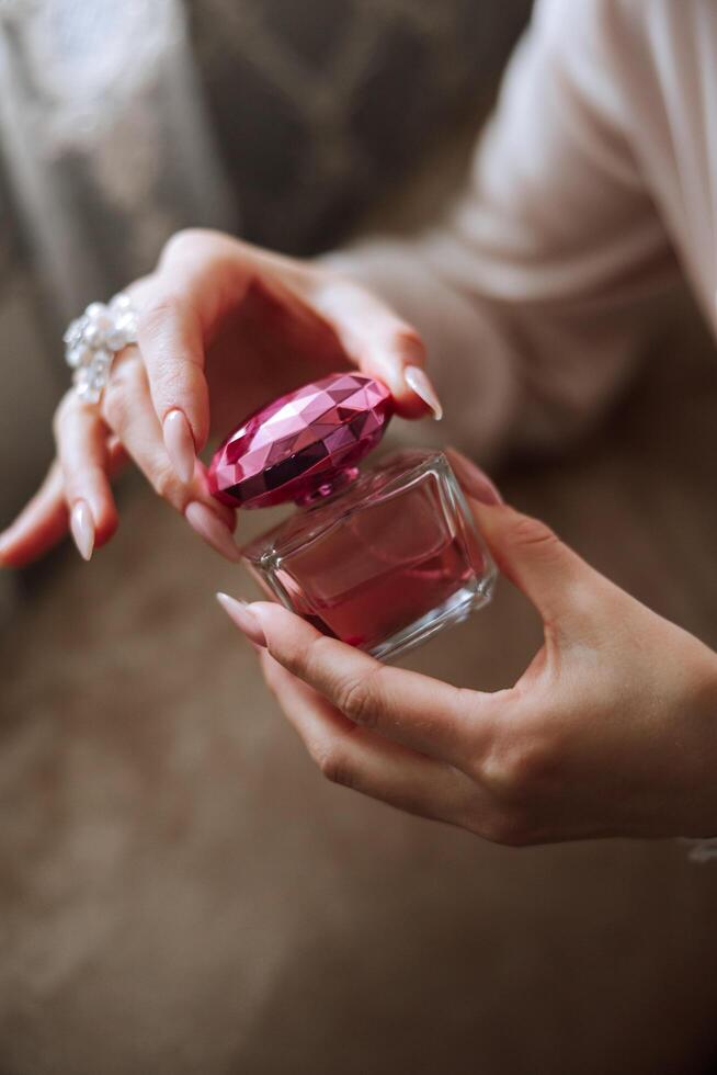 roze parfum fles in inschrijving vrouw handen. de bruid sprays parfum Aan haar lichaam. detailopname foto. manicuren. ochtend- van de bruid. foto