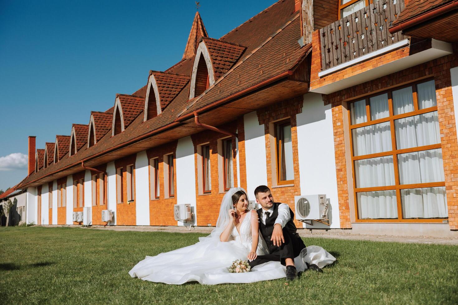 mooi paar zittend en knuffelen buitenshuis Aan hun bruiloft dag, ontspannende Aan de het beste zomer dag. een knap bruidegom en een elegant bruid in een prachtig bruiloft jurk. foto