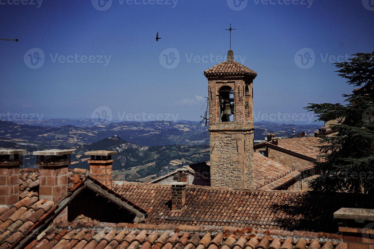 de steen klok toren is omringd door betegeld daken, de atmosfeer van de Italiaans zomer foto