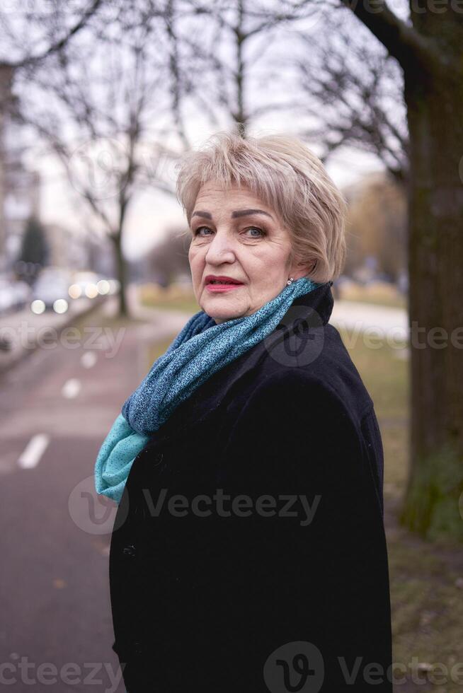 portret van een elegant oud vrouw in een zwart jas met groen accessoires Aan een voorjaar straat foto