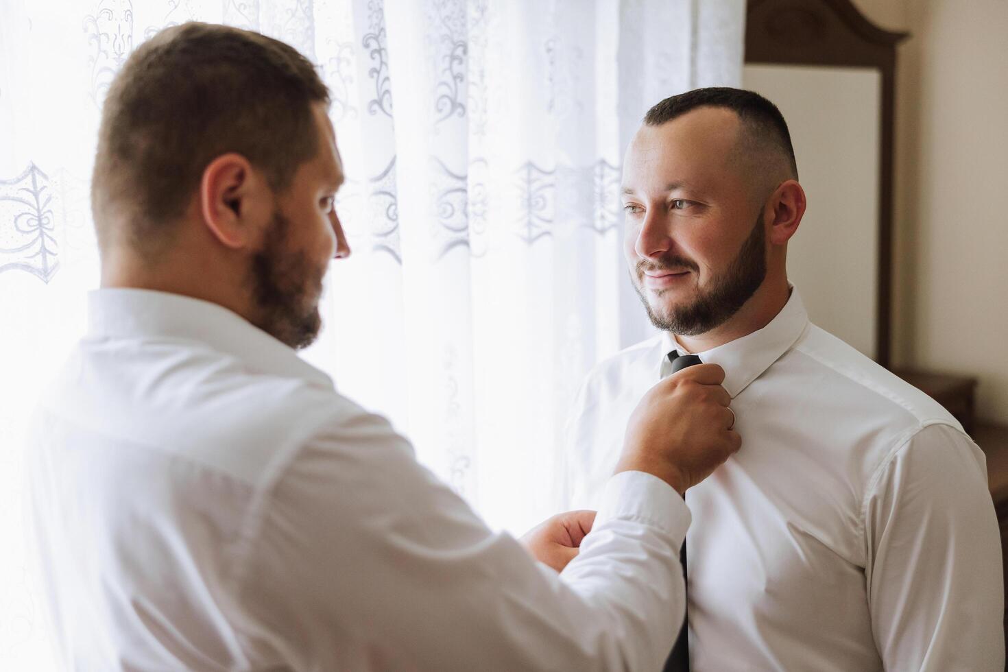 elegant bruidegom lachend en hebben pret met bruidsjonkers terwijl krijgen klaar in de ochtend- voor bruiloft ceremonie. luxe Mens foto