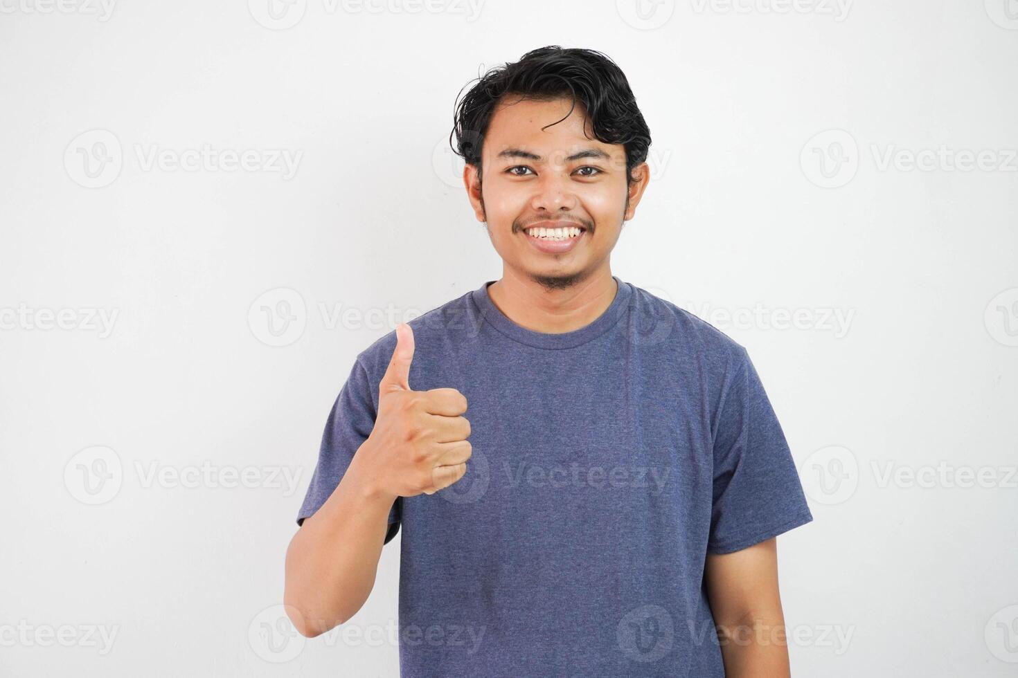 jong knap Aziatisch Mens vervelend gewoontjes met wit achtergrond aan het doen gelukkig duimen omhoog gebaar met hand. goedkeuren uitdrukking op zoek Bij de camera tonen succes. foto