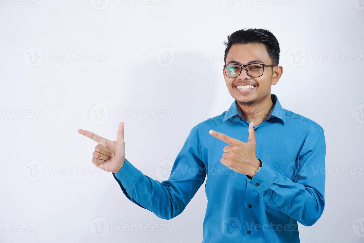 knap Aziatisch mannetje werknemer met bril glimlachen in een houding vinger richten naar de kant vervelend blauw overhemd geïsoleerd Aan wit achtergrond foto