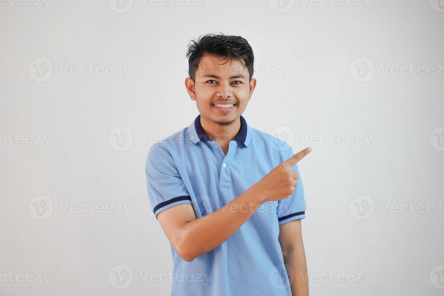 glimlachen Aziatisch Mens met vingers richten naar de kant vervelend blauw t overhemd geïsoleerd Aan wit achtergrond foto