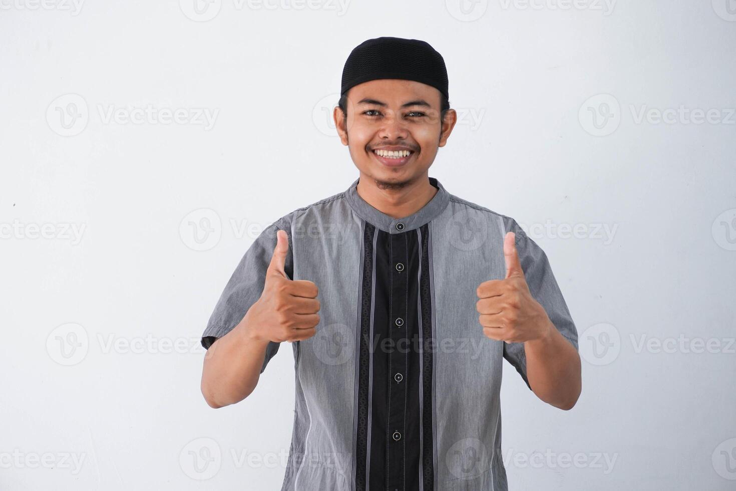 glimlachen of gelukkig jong moslim Mens tonen hand- duimen omhoog vervelend grijs moslim kleren geïsoleerd Aan wit achtergrond foto