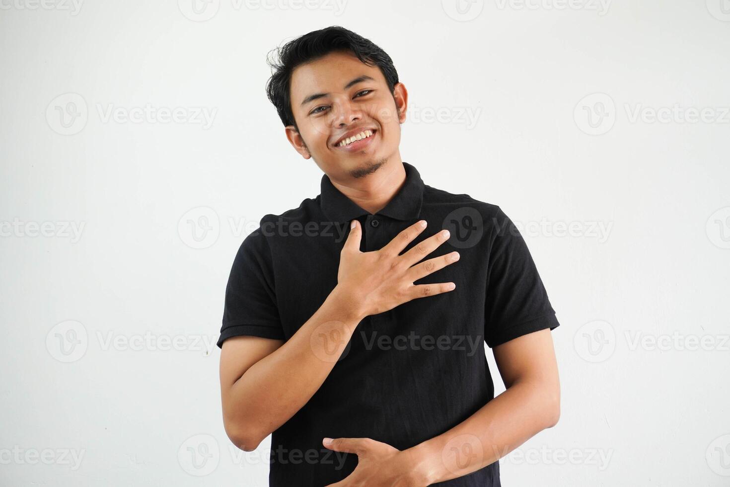 glimlachen jong Aziatisch Mens lacht gelukkig en heeft pret houden handen Aan borst en maag vervelend zwart polo t overhemd geïsoleerd Aan wit achtergrond foto