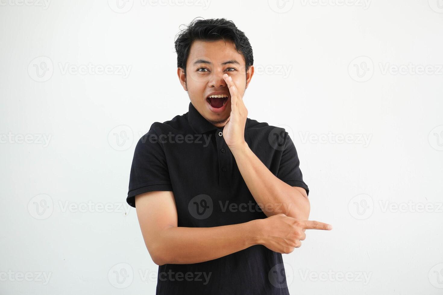 jong Aziatisch Mens poseren Aan een wit backdrop gezegde een geroddel, richten naar kant rapportage iets, vervelend zwart polo t shirt. foto