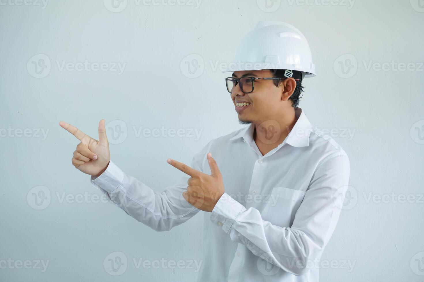 jong Aziatisch architect Mens vervelend wit moeilijk hoed veiligheid helm op zoek camera met vinger richten de Rechtsaf kant geïsoleerd Aan wit achtergrond foto