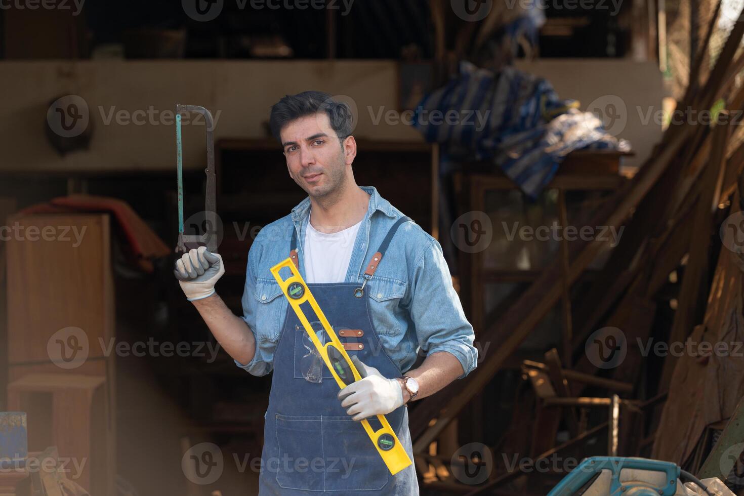 portret van een timmerman Holding een geest niveau en handzaag in zijn werkplaats. foto