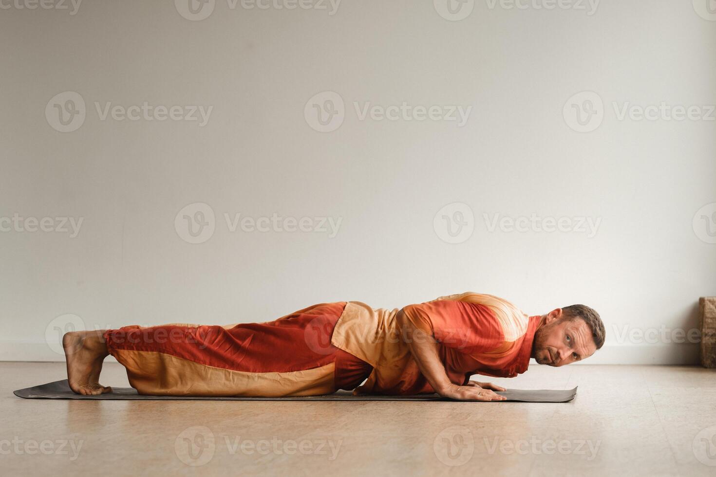 een Mens in een oranje pak doet yoga in een geschiktheid kamer. de concept van Gezondheid foto