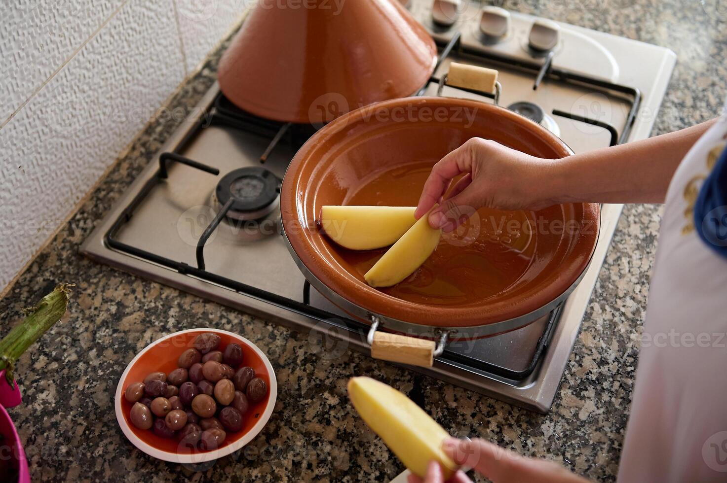 top visie van een huisvrouw Koken tajine, zetten plakjes van biologisch aardappel binnen een klei gerecht. Marokkaans traditioneel voedsel foto