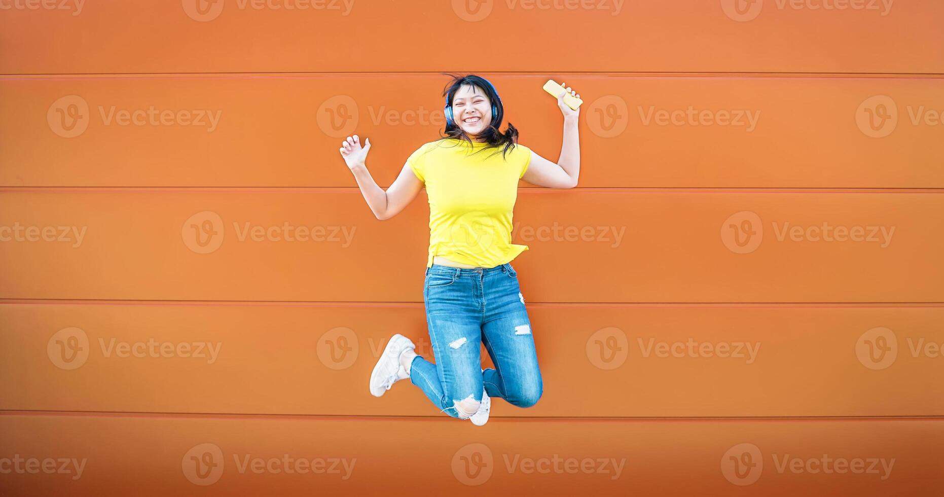 gelukkig Aziatisch meisje jumping terwijl luisteren muziek- met draadloze hoofdtelefoons - gek Chinese vrouw hebben pret dansen buitenshuis - jeugd millennial generatie levensstijl mensen en technologie concept foto