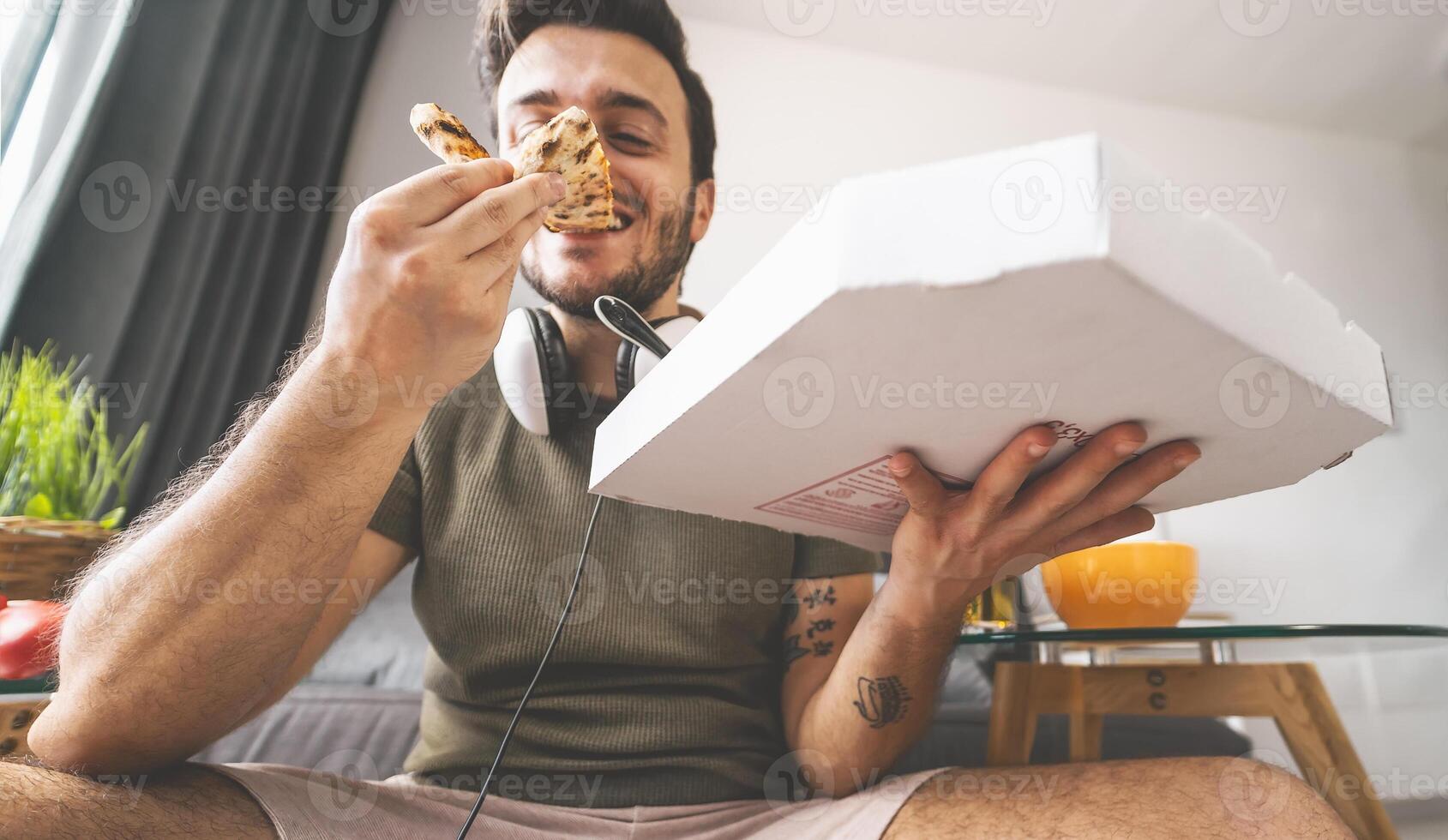 jong Mens aan het eten pizza levering Bij huis - gelukkig vent hebben maaltijd terwijl spelen video spellen in leven kamer - voedsel en jeugd mensen vermaak concept foto