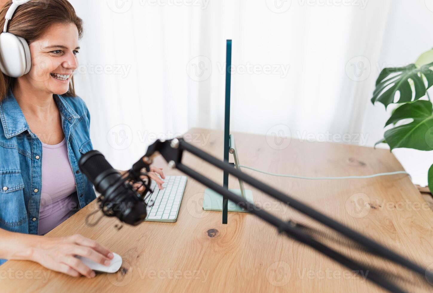 gelukkig vrouw opname een podcast gebruik makend van computer en microfoon van haar huis studio foto