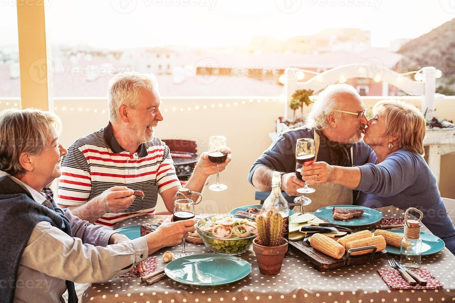 gelukkig senior vrienden dining en juichen met rood wijn Bij barbecue in terras buitenshuis - gepensioneerd mensen hebben pret Bij bbq partij Aan patio - vriendschap, voedsel en ouderen levensstijl concept foto