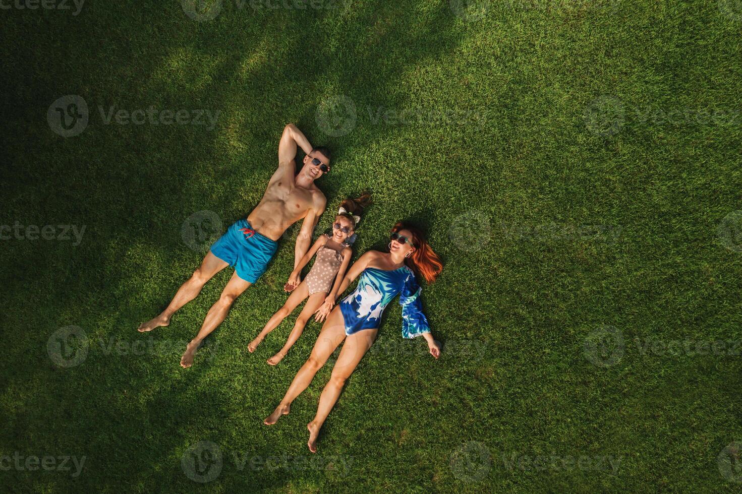 top visie van een gelukkig familie in zwemkleding aan het liegen Aan de groen gras foto