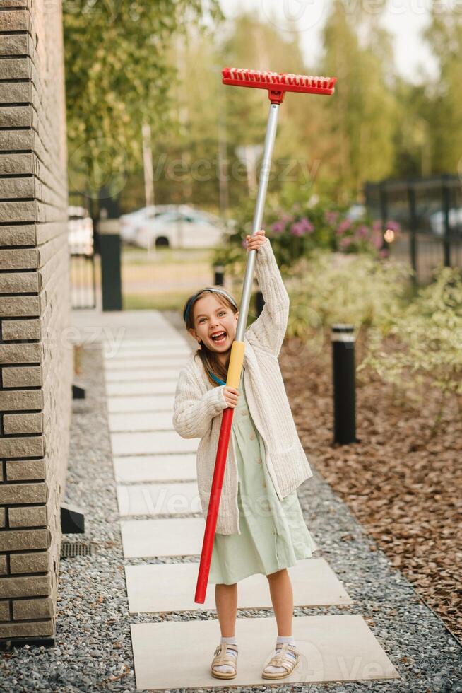 een weinig meisje met een borstel reinigt een pad Aan de straat in de binnenplaats foto