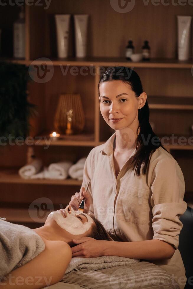 een schoonheidsspecialist maakt een masker voor een vrouw gezicht naar verjongen de huid. schoonheidsspecialiste foto