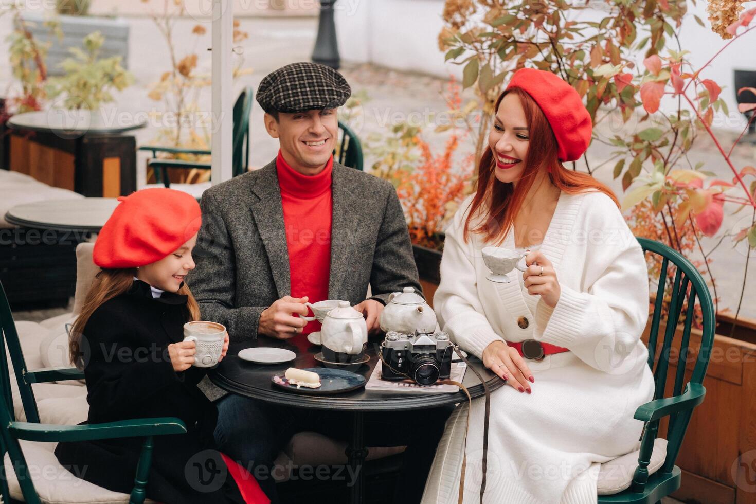 een elegant familie verzameld samen in een cafe Aan de straat. mama, pa, weinig dochter drinken thee, eten taarten. ze zijn gelukkig samen. de concept van een gelukkig familie avondeten foto