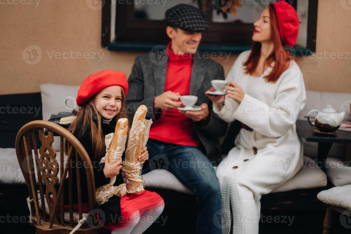 een elegant familie van drie is zittend Bij een tafel buiten in een cafe en drinken koffie. pa, mam en dochter in de herfst stad foto