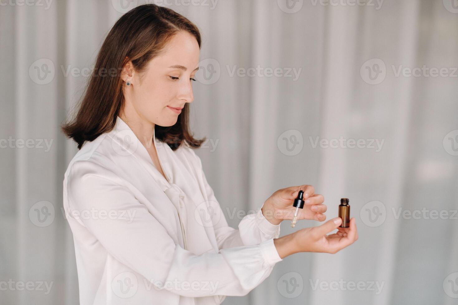 een meisje met een wit blouse houdt essentieel oliën in haar handen en druppelt Aan haar pols foto