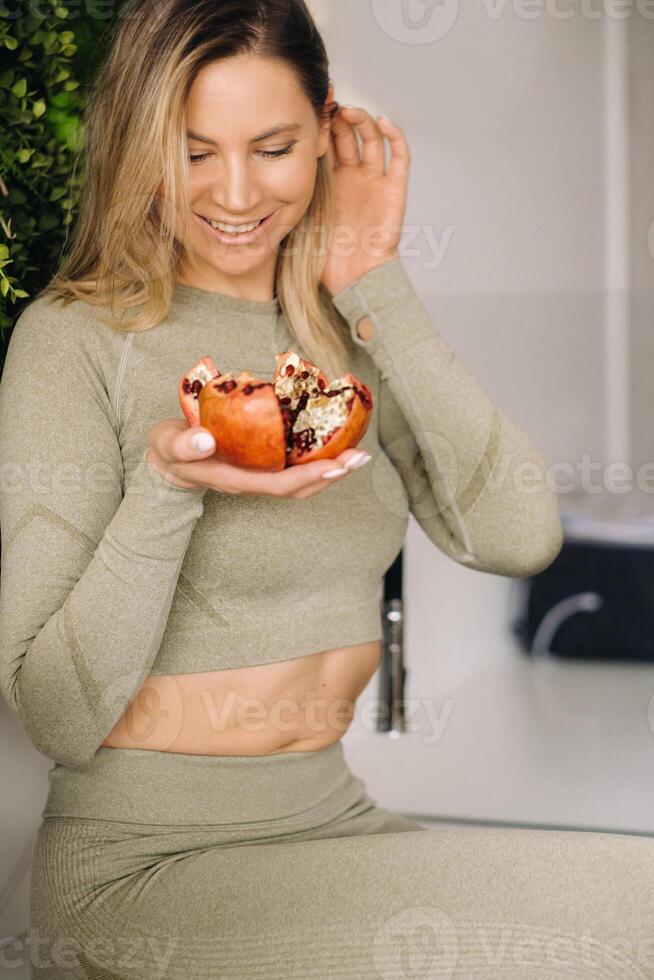 een sportief vrouw in sportkleding houdt een granaat in haar hand. de concept van gezond aan het eten foto