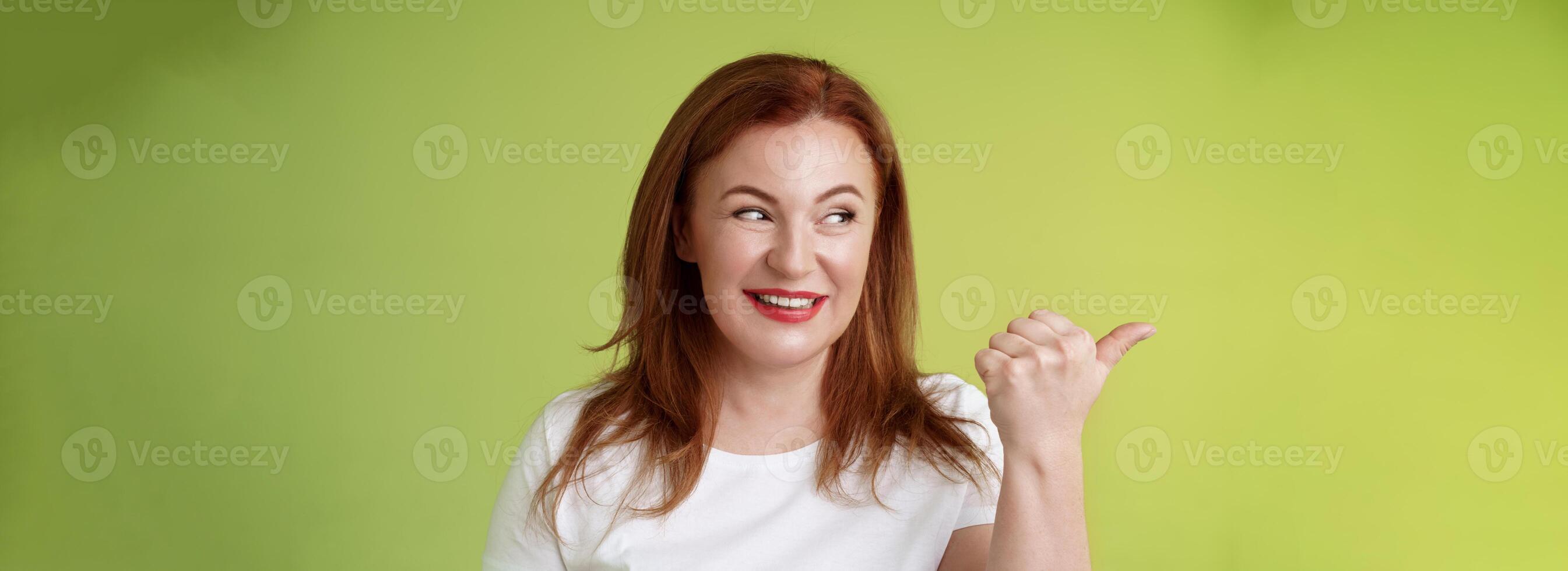 gefascineerd charismatisch roodharige middelbare leeftijd vrouw glimlachen verleiding interesseren richten op zoek links merkwaardig uitchecken koel promo delen geweldig plaats plaats staan groen achtergrond foto