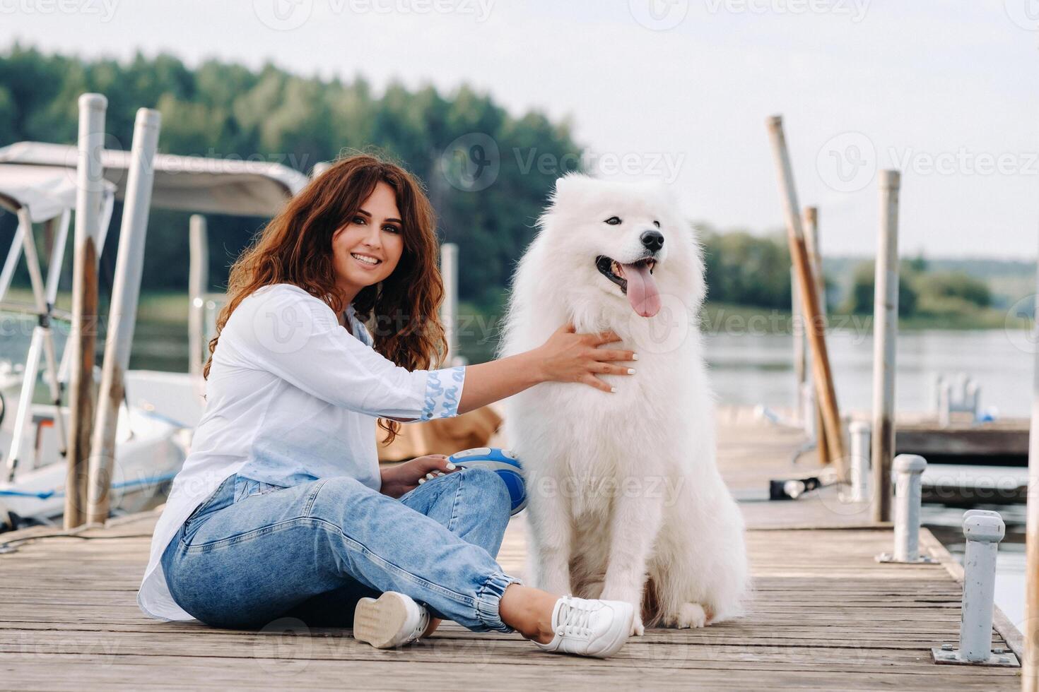 een gelukkig vrouw met een groot wit hond leugens Aan een pier in de buurt de zee Bij zonsondergang foto