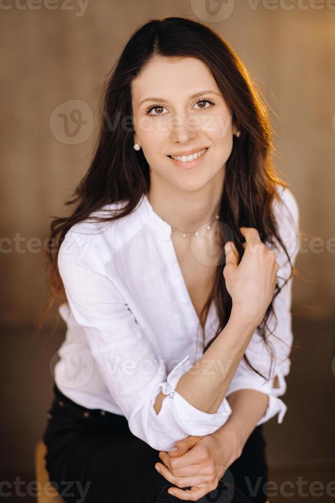 portret van een gelukkig jong brunette vrouw in een wit overhemd zittend Aan een stoel foto