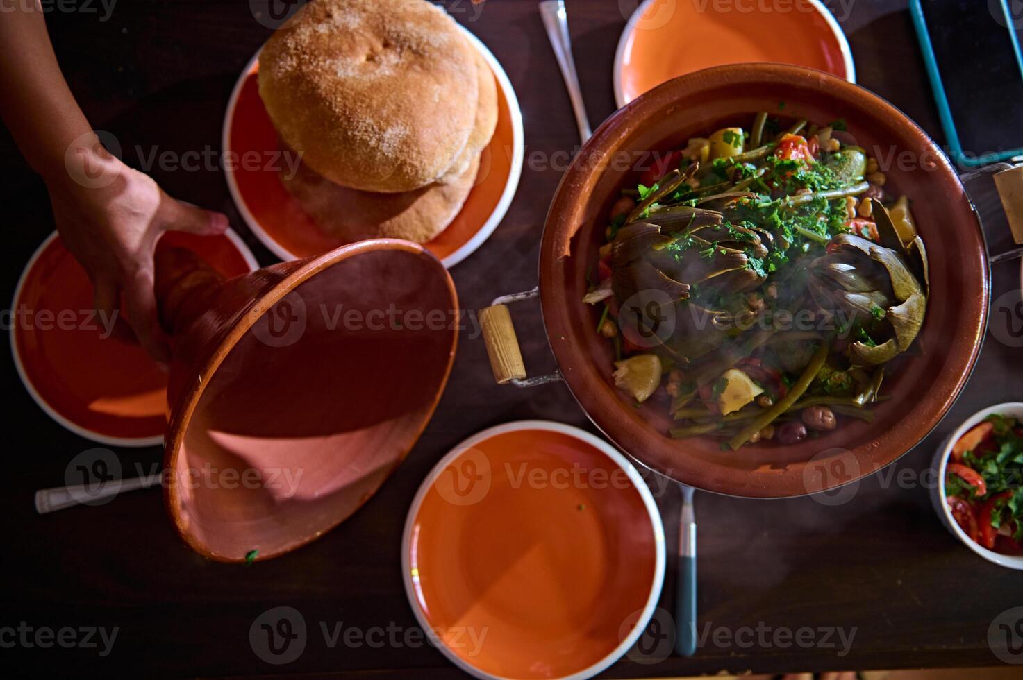 direct bovenstaand opening deksel van klei servies, tonen een vegetarisch maaltijd met biologisch groenten gestoomd in tajine met stoom- foto