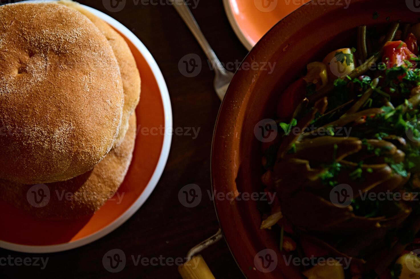 top visie van vers gebakken volkoren brood Aan keramisch bord. en tajine met gestoomd groenten Aan een houten tafel. voedsel blog foto