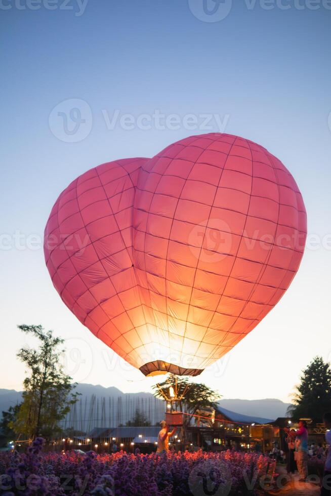 hart vormig heet lucht ballon drijft over- veld- van bloemen in avond, en hart vormig ballonnen zijn ook symbool van liefde en vriendschap. gebruik makend van hart vormig ballonnen net zo symbool van liefde en vriendschap. foto