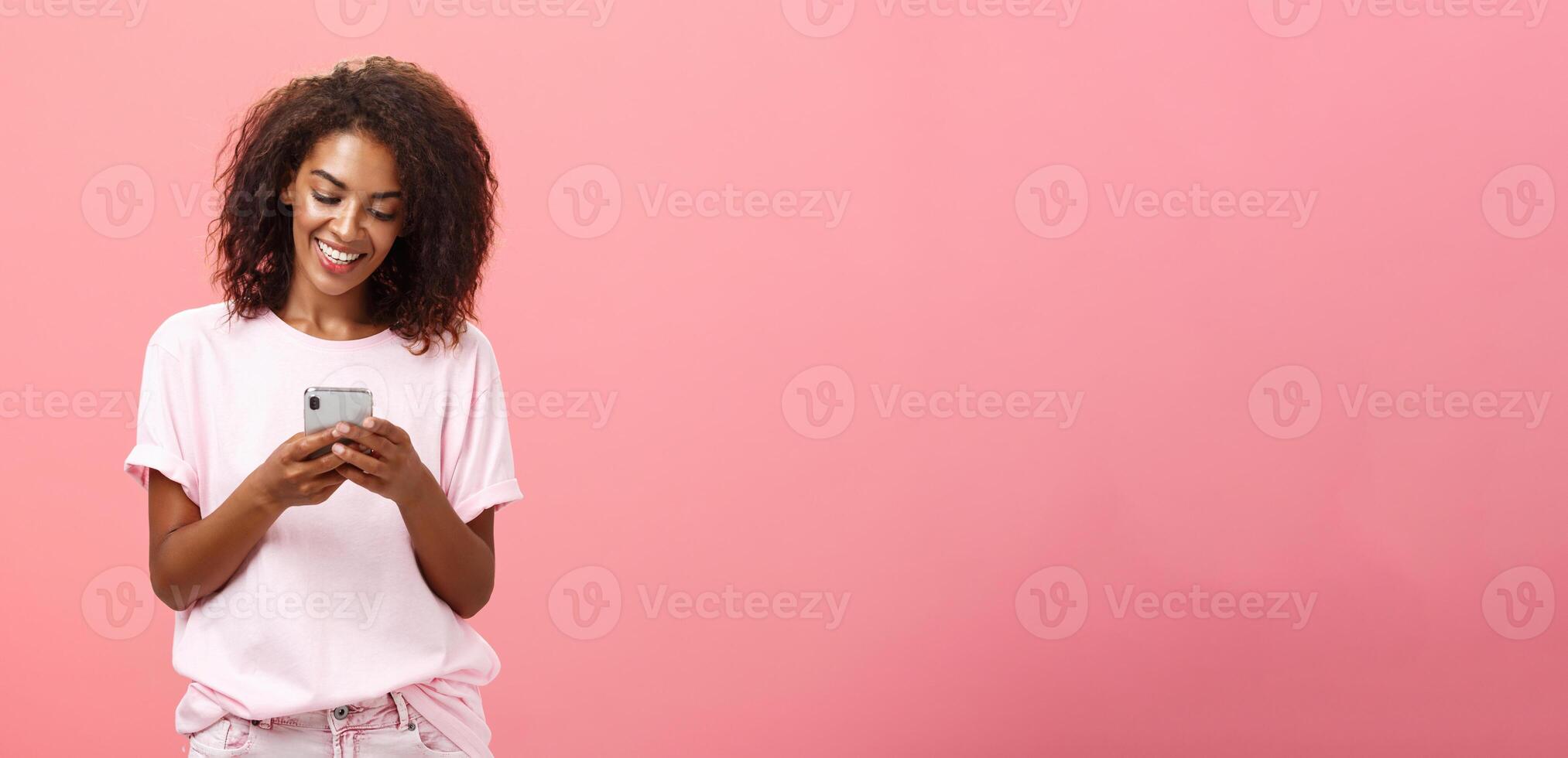 meisje schrijven tekst bericht naar vriend. portret van charmant geamuseerd en gelukkig jong met een donkere huid vrouw met gekruld haar- op zoek Bij smartphone scherm typen glimlachen genieten van koel Kenmerken van mobiele telefoon foto