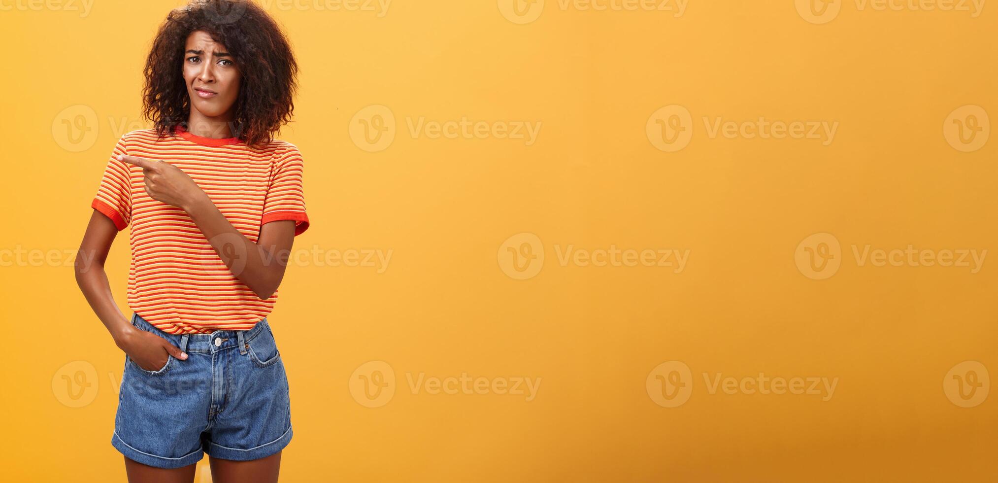 niet waard mijn tijd. niet tevreden niet onder de indruk elegant aantrekkelijk met een donkere huid vrouw model- in gestreept t-shirt en denim shorts fronsen met kieskeurig uitdrukking richten links twijfelachtig en ontevreden foto