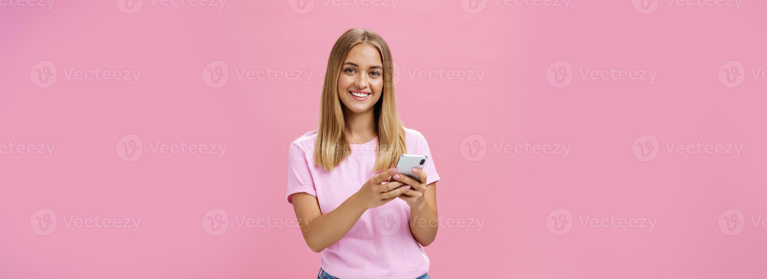 vrouw roeping taxi's via smartphone vragen vriend adres glimlachen vrolijk Bij camera Holding telefoon met beide handen over- borst krijgen in tintje met klanten via berichten staand over- roze muur foto