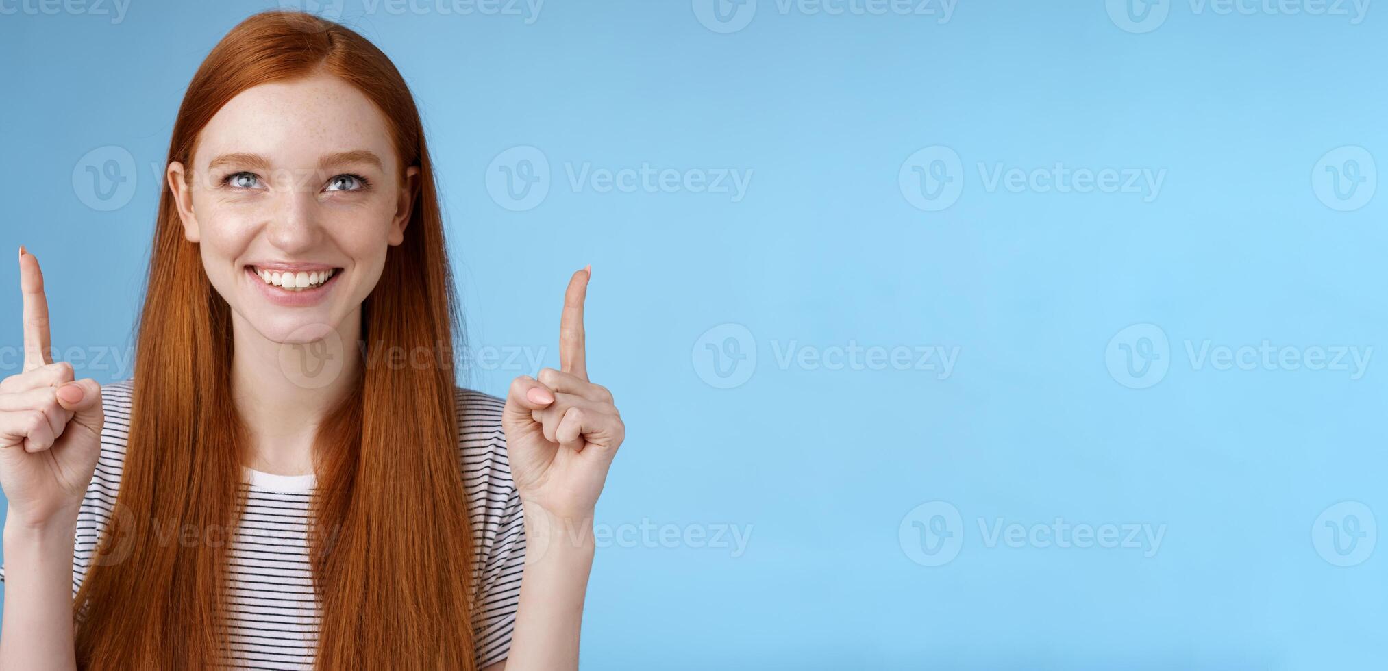 geamuseerd opgewonden gelukkig glimlachen roodharige meisje kijken richten omhoog grijnzend graag aan het kijken geweldig Open lucht prestatie staand blij tonen koel ding wijzend op Product, blauw achtergrond foto