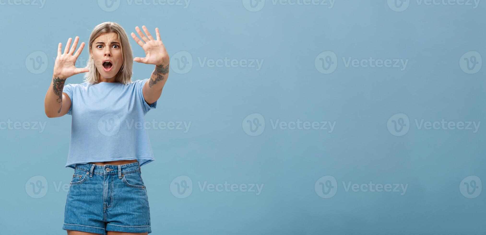 vrouw doodsbang schreeuwen en vragen hou op. portret van geschokt in paniek raken verontrust blond vrouw in denim shorts en gewoontjes t-shirt trekken handen in Nee gebaar dropping kaak en fronsen foto