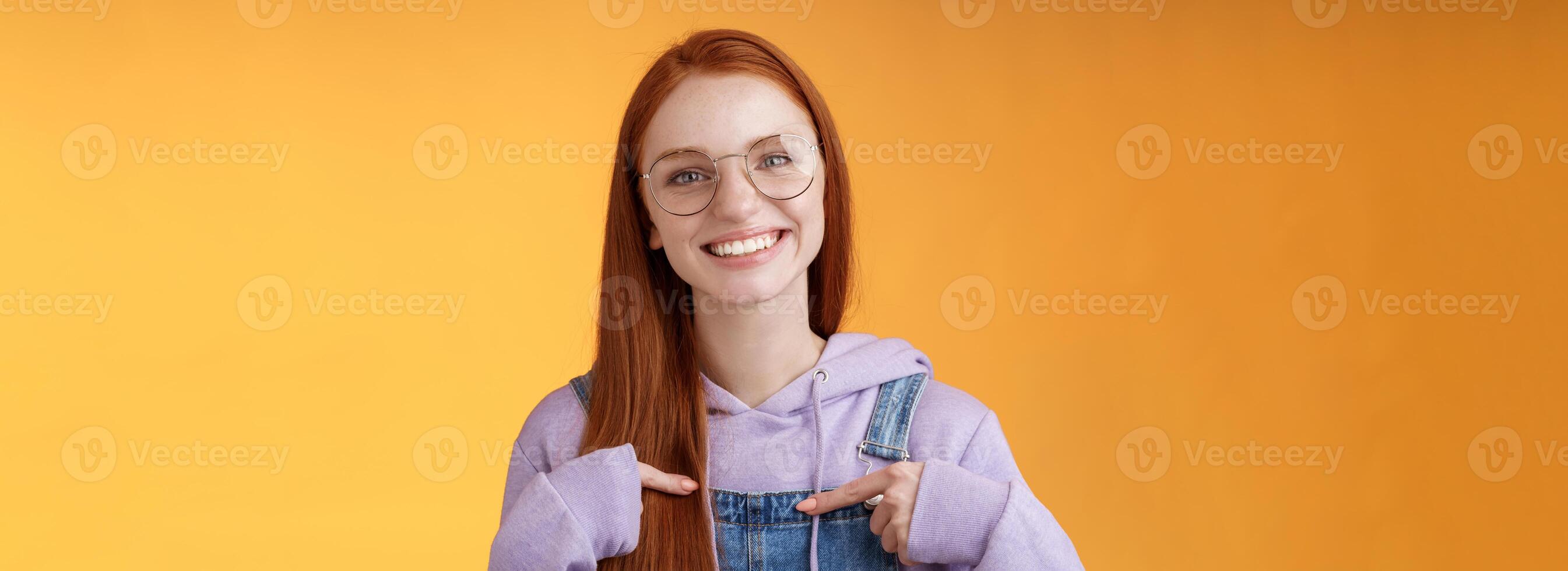 gelukkig levendig vriendelijk roodharige Europese meisje richten haarzelf suggereren helpen opscheppen vertellen eigen prestaties glimlachen wit tanden verheugd vrijwilligerswerk, wezen geplukt, oranje achtergrond foto